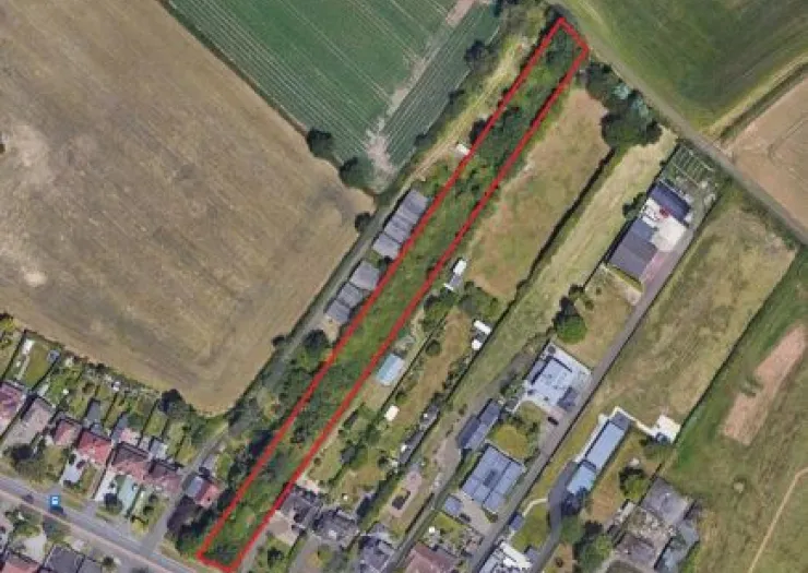 Aerial view of a narrow, red-outlined land parcel amidst fields and buildings.
