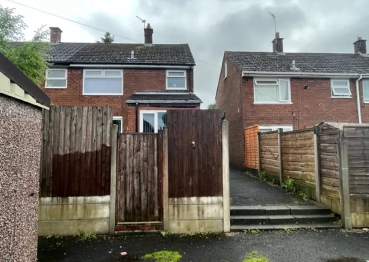 Rear view of a brick house with a gated wooden fence and driveway.