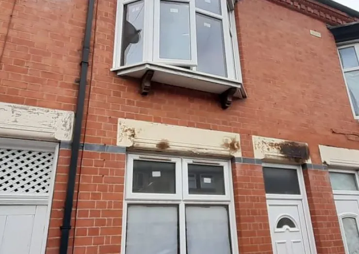 Red brick house exterior with bay window and peeling paint above ground floor windows.