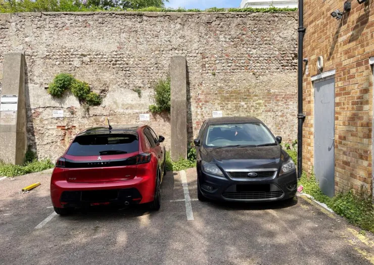 Two cars parked in an off-street parking lot by a brick wall.
