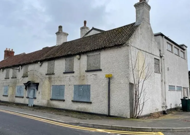 Boarded-up white two-story building with multiple chimneys and tiled roof.