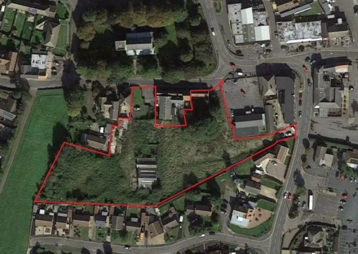 Aerial view of land outlined in red, showing buildings, vegetation, and adjacent roads.
