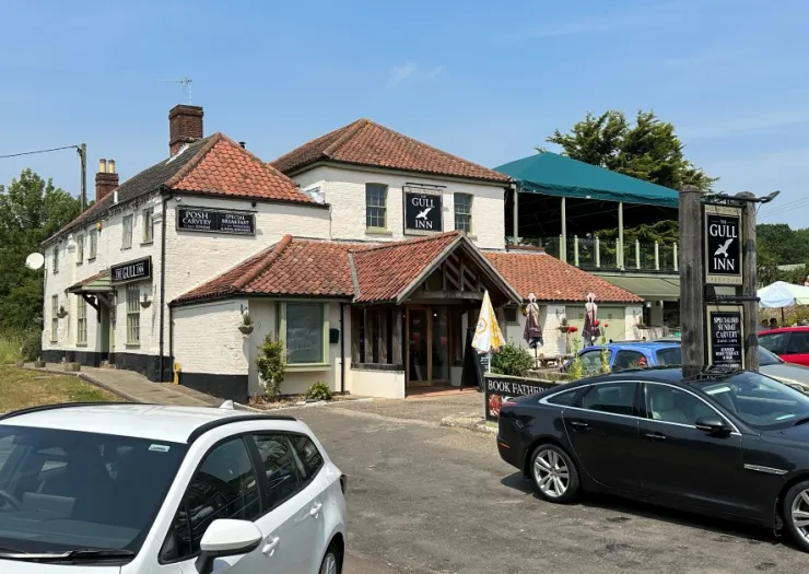 The Gull Inn, a white and terracotta pub, with cars parked outside and a covered patio area.