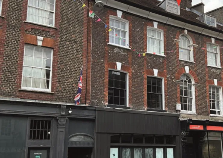 Brick building with dark storefronts and Union Jack flag. Upper levels have multi-paned windows and festive bunting.