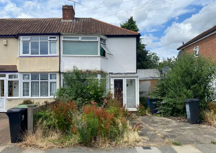 Semi-detached house with overgrown front garden and driveway.
