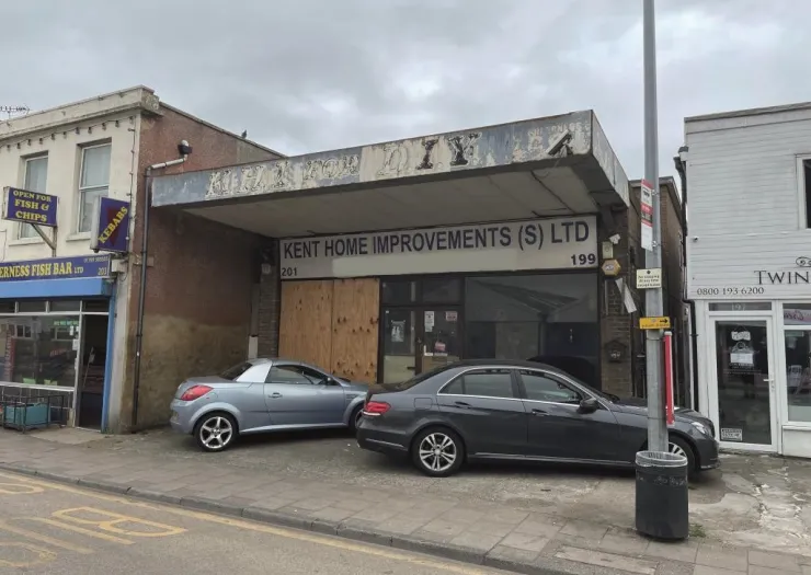 Kent Home Improvements (S) LTD storefront with boarded-up windows, parked cars, and adjacent businesses.