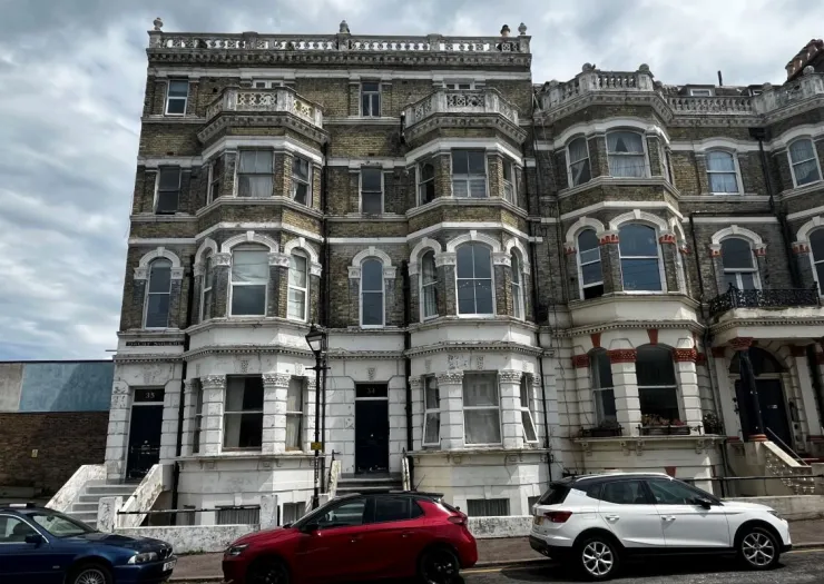 Grand Victorian apartment building with bay windows and decorative white trim, parked cars on street.
