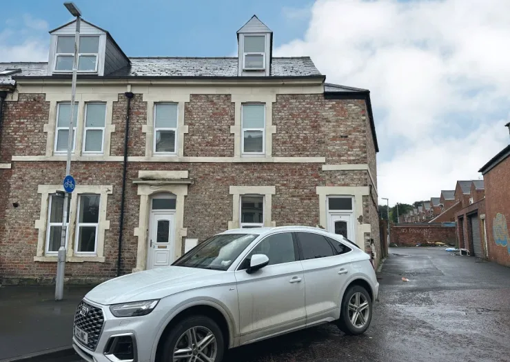 Brick terraced house with dormer windows and a parked car in front.
