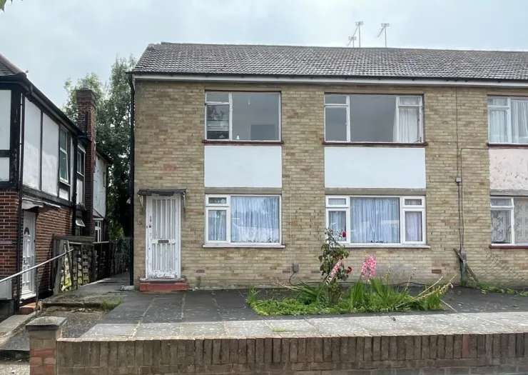 Exterior of a two-story yellow brick apartment building with white-framed windows and a gated front door.