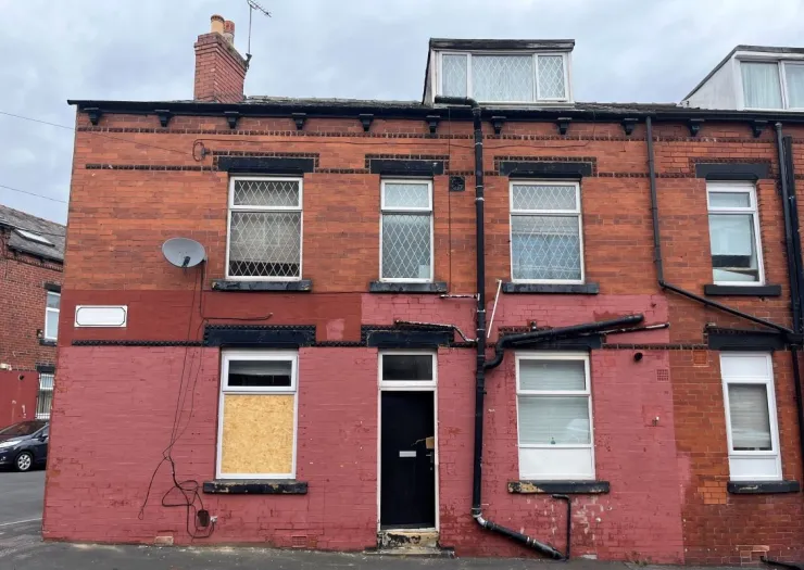 Red brick terraced house with boarded-up ground floor window.