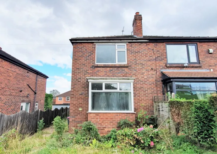Red brick semi-detached house exterior with white and dark framed windows. Overgrown front garden.
