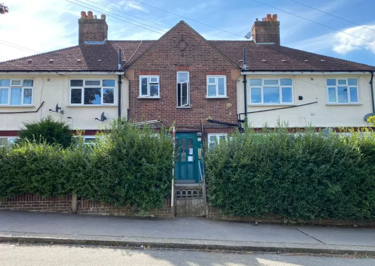 Brick apartment building with green entryway and hedge.