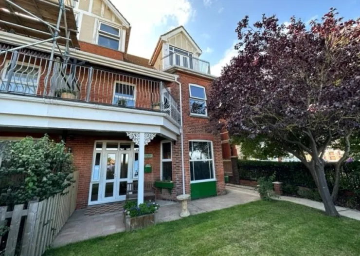Red brick house with white trim, balconies, and a purple-leafed tree in the garden.
