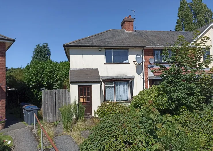 Semi-detached house with overgrown front garden and driveway.