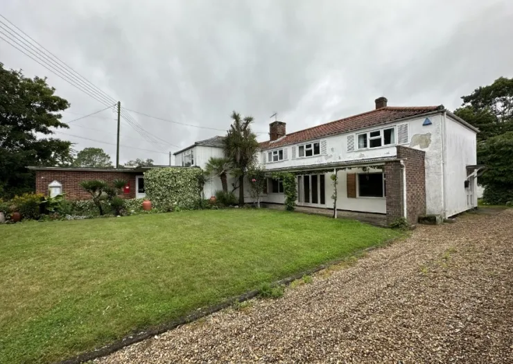 White detached house with red tiled roof, covered porch, and gravel driveway, viewed from the front garden.