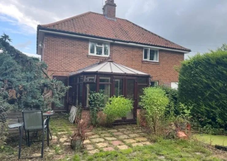 Red brick house with brown conservatory and overgrown garden.