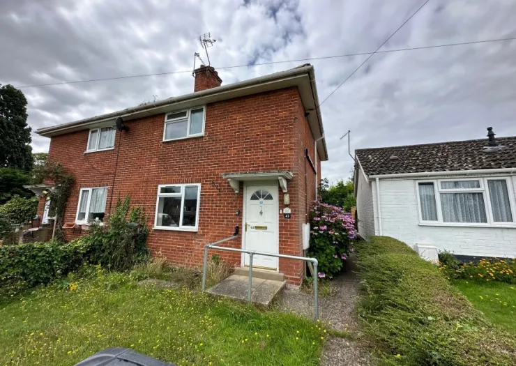 Red brick house exterior with white door, access ramp, and front garden.