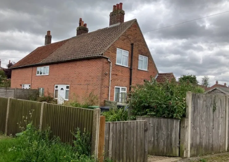 Red brick house with tiled roof, white windows, and wooden fenced yard.