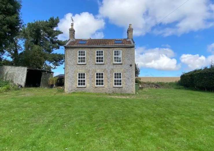 Stone farmhouse with white-framed windows, two chimneys, and a green lawn under a blue sky.