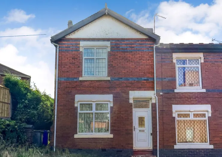 Red brick terraced house exterior with white windows and door, under a blue sky.
