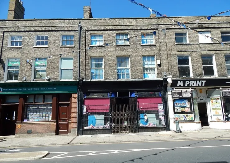 Brick storefronts with "Bycroft" real estate office and "M Print" shop on sunny street.