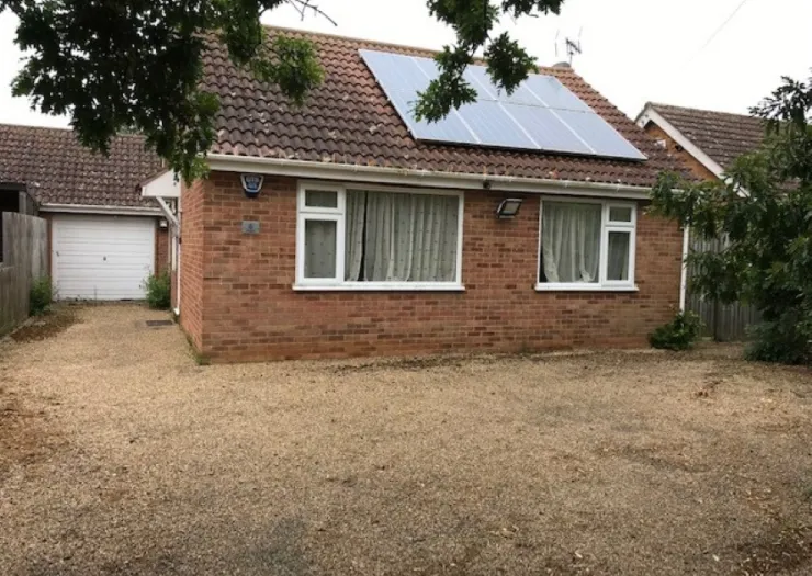 Red brick bungalow with solar panels, white windows, and gravel driveway.