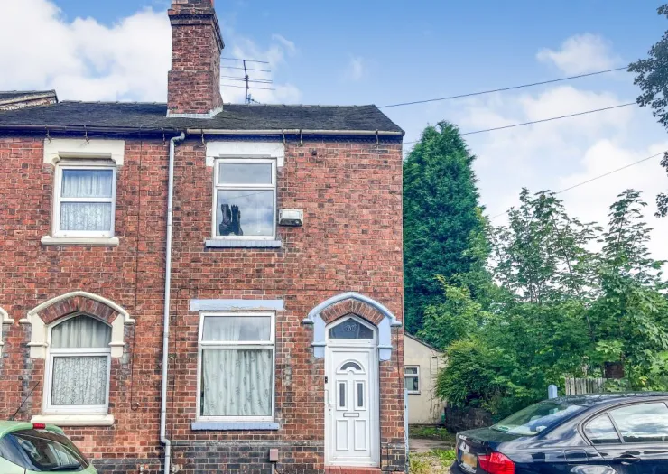 Red brick terraced house exterior with white front door, visible windows, and green trees in the background.