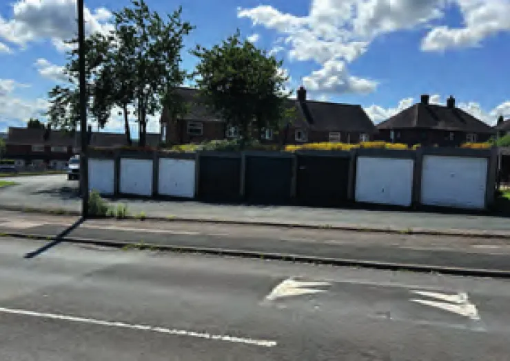 Row of garages behind houses, seen from across the road.