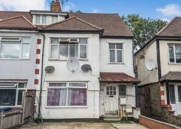 White semi-detached house with tiled roof, multiple windows, and satellite dishes.