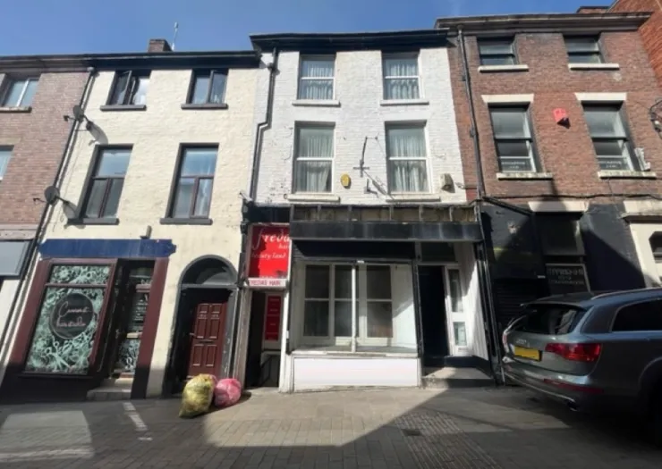 White and brick multi-story commercial building with empty storefront.