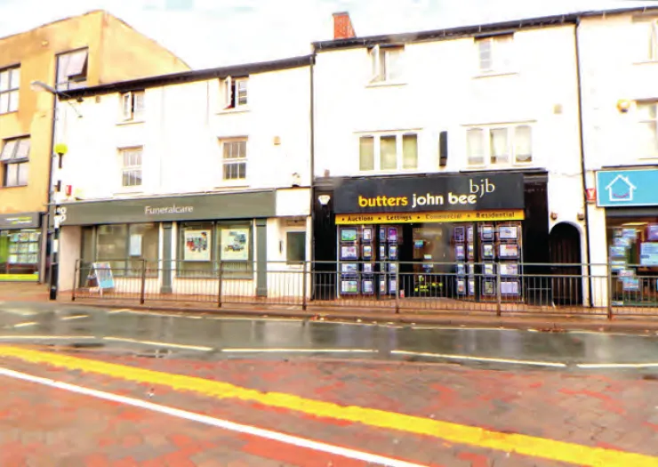 Butters John Bee estate agents storefront with property listings displayed. Adjacent is Funeralcare. Wet street.