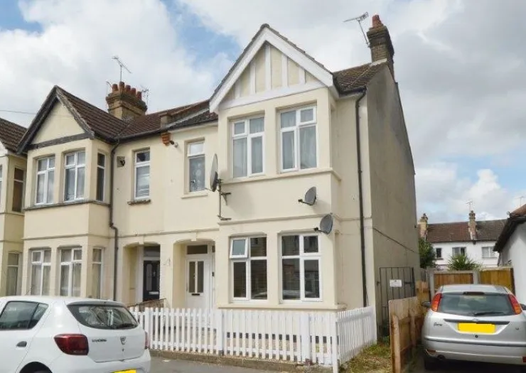 Cream-colored semi-detached house with white picket fence and parked cars.