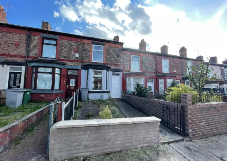 Red brick terraced house with bay window and driveway, under a blue sky.