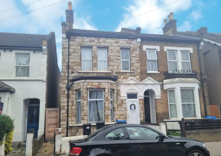 Stone & brick terraced house exterior with bay window and parked car.