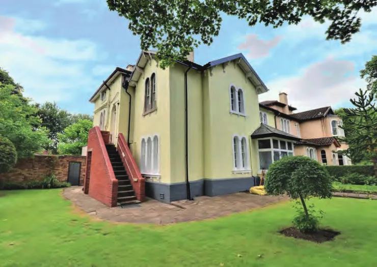 Pale yellow Victorian house exterior with red brick staircase, viewed from a green lawn.
