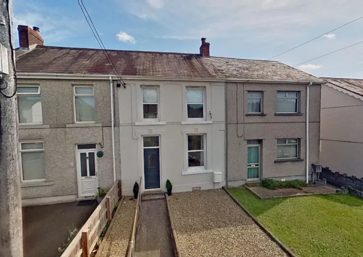 Terraced house exterior with gravel driveway and accessible ramp to front door.