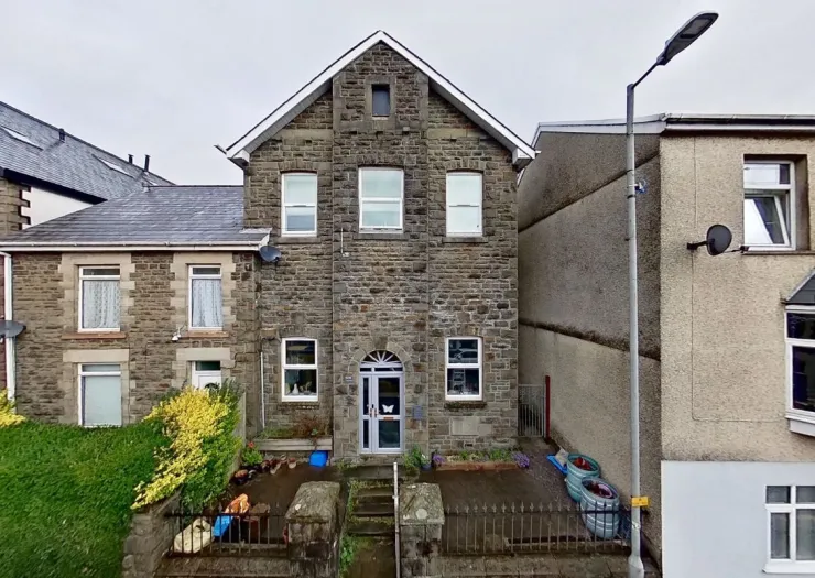 Stone terraced house exterior with grey roof, front garden, and gated entrance.