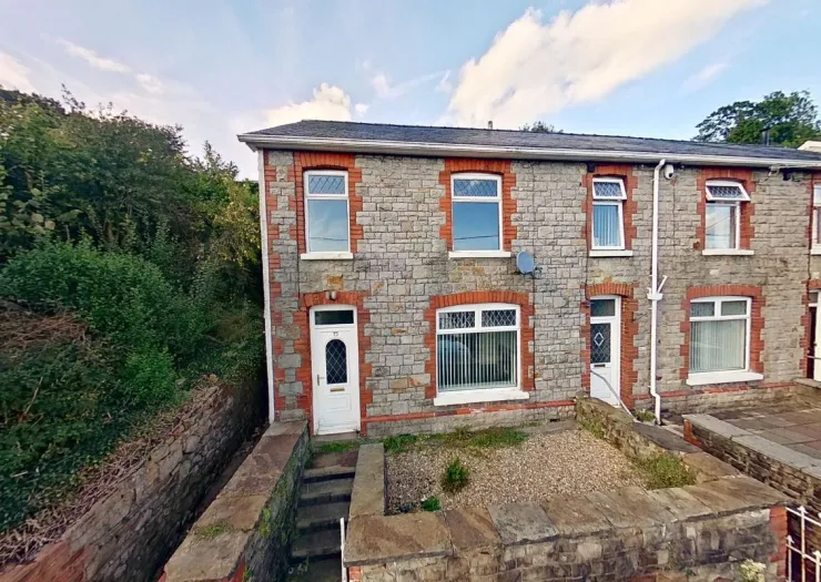 Stone terraced house with red brick accents, white windows, and front garden.