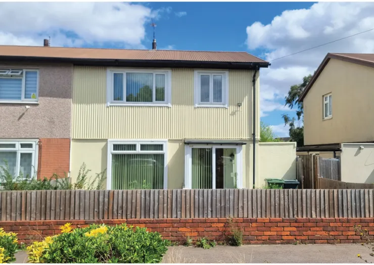 Cream two-story house with corrugated siding, front garden, and wooden fence.