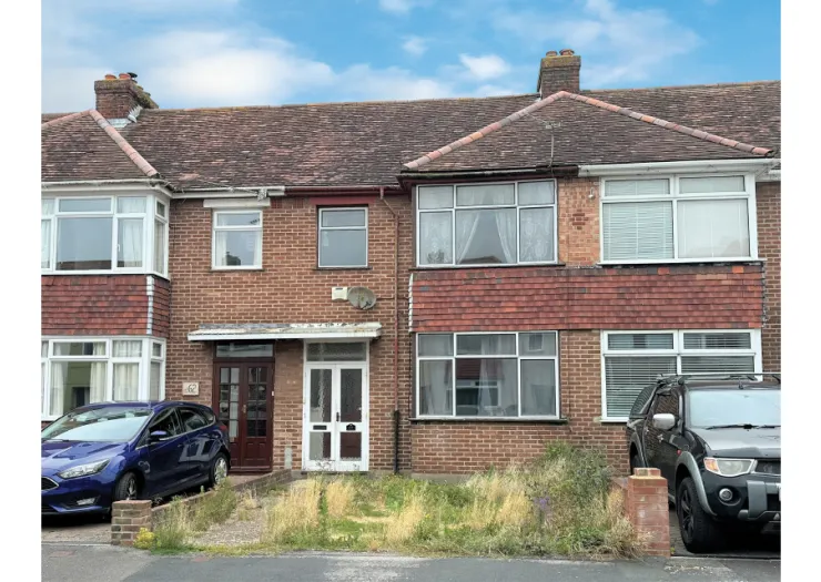 Attached brick house exterior with bay windows, overgrown front garden, and parked cars.