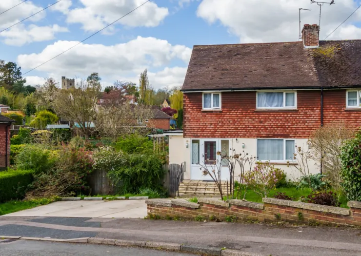 Red brick house with front garden and driveway, village church in background.