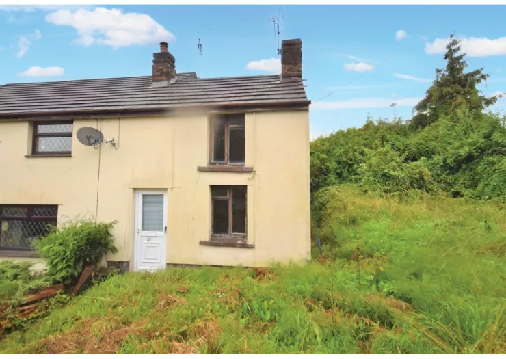 Small yellow terraced house with overgrown front yard.