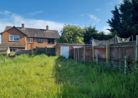 overgrown back garden with exterior of brown brick house at the end