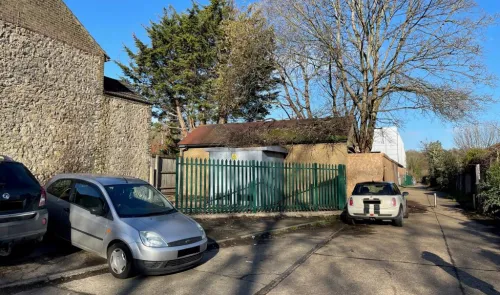 Cars parked near a fenced electrical substation and a stone building.