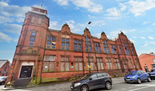 Large red brick building with boarded-up windows and a small tower under a blue sky.
