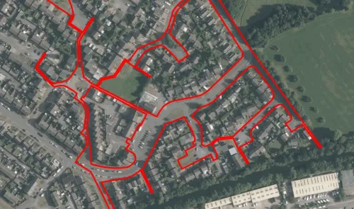 Aerial view of a residential area outlined in red, showing houses, roads, and green spaces.