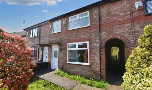 Red brick terraced house exterior with white door and windows, walkway, and arched side passage.