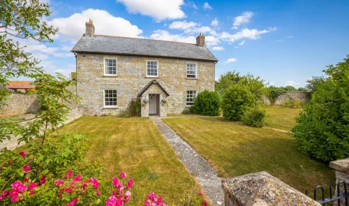 Charming stone farmhouse with front garden, pathway, and vibrant pink roses.
