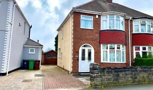 Red brick house with bay windows, white front door, driveway, and small front garden.