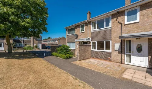 Attached house exterior with brown brick, white door, and small paved front yard on a sunny day.